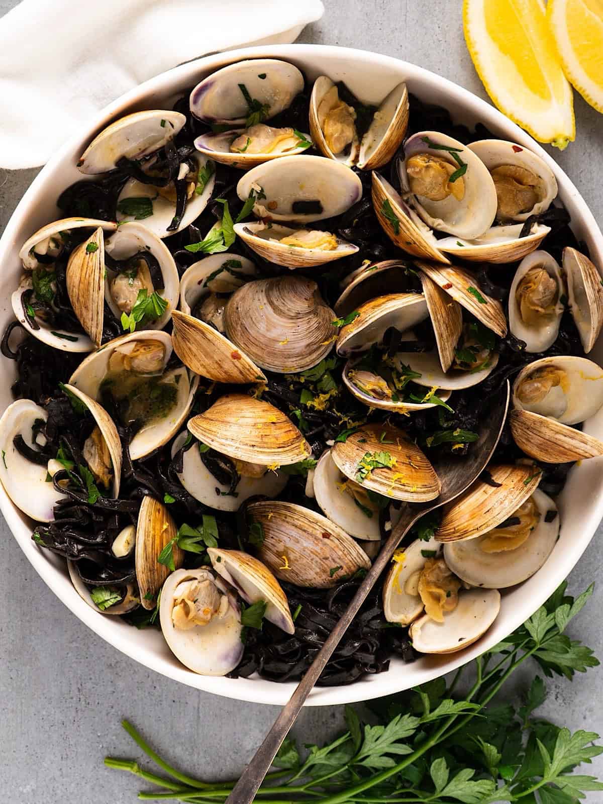 Linguine nero di seppia in serving bowl with garnish and lemon wedges.