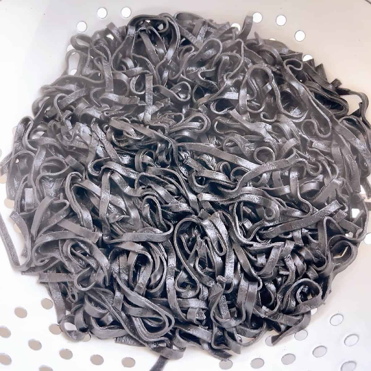 Boiled linguine nero di seppia in a colander draining.