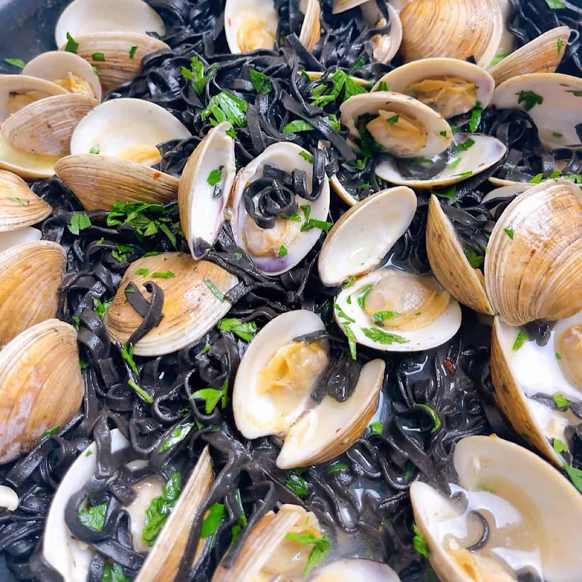 Black pasta combined with the clams and sauce garnished with parsley.
