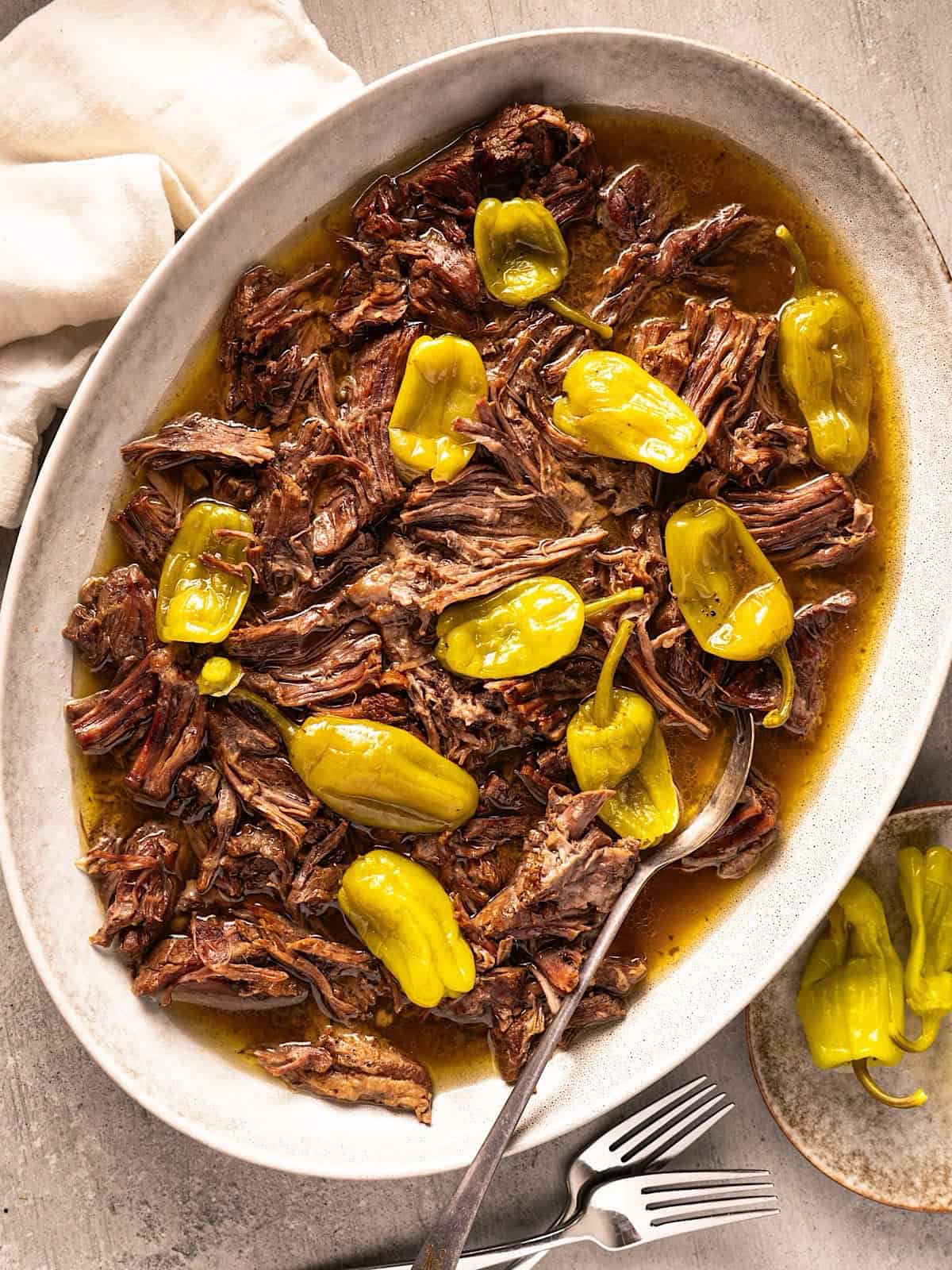 Easy instant pot mississippi pot roast recipe with pepperoncini on a platter with serving spoon.