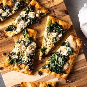 Sliced flatbread pizzas with spinach and feta on a cutting board.