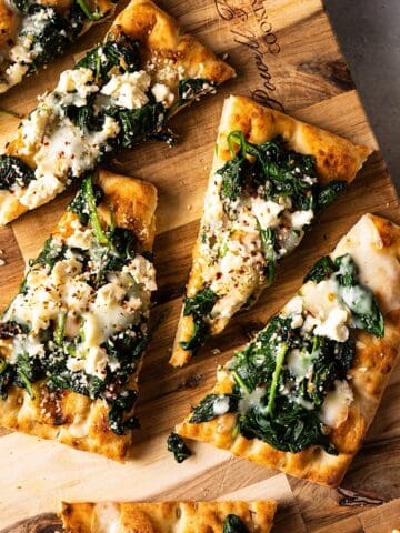 Sliced flatbread pizzas with spinach and feta on a cutting board.