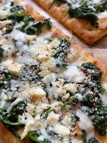 Two flatbread pizzas with spinach and feta on a cutting board.