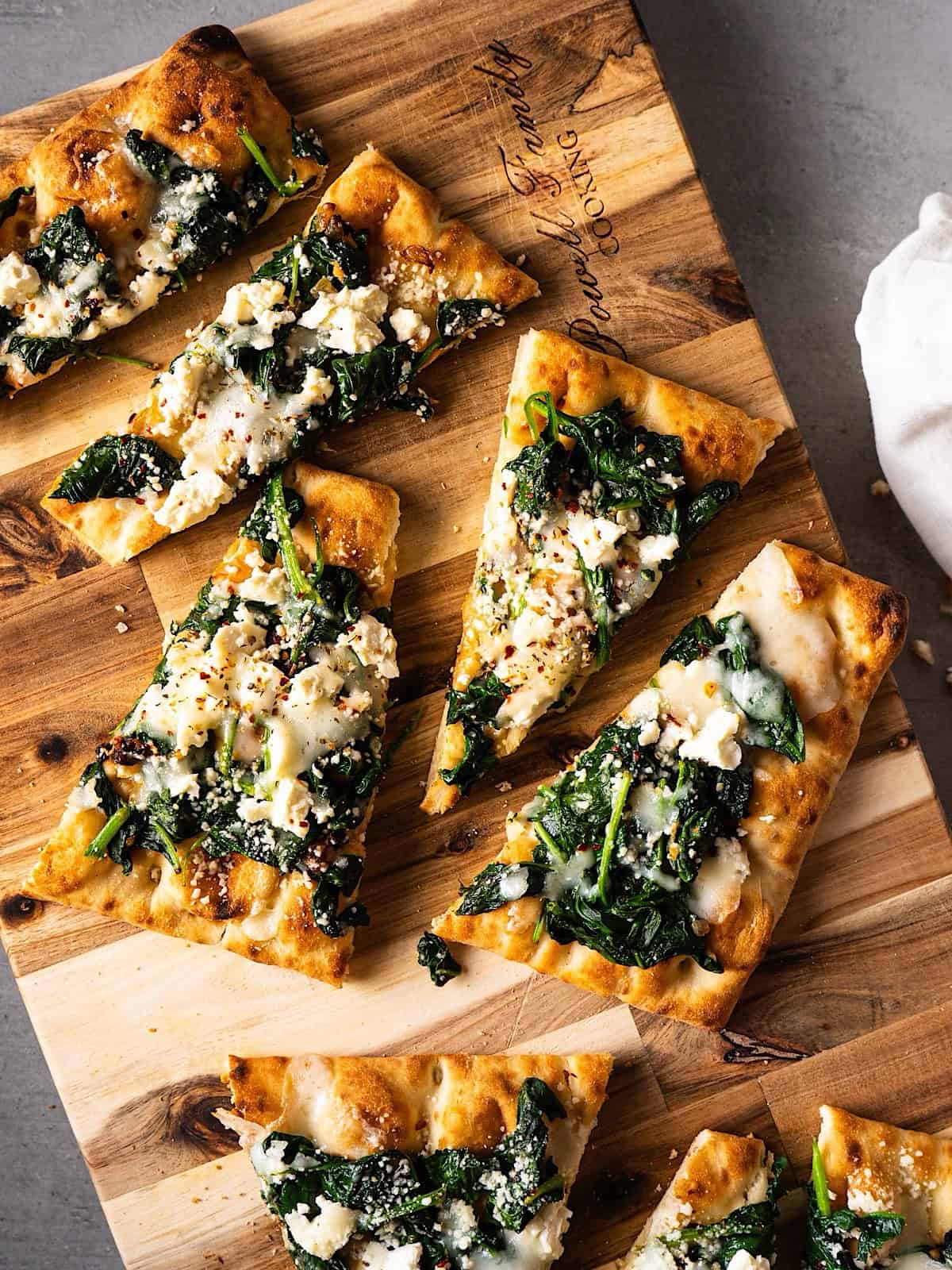 Sliced flatbread pizzas with spinach and feta on a cutting board.