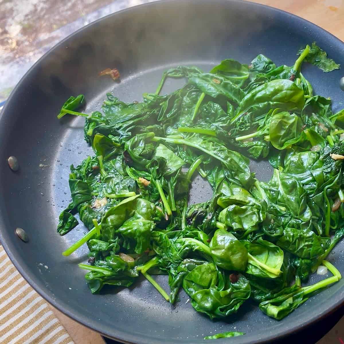Caramelized onions sauteeing with fresh spinach.