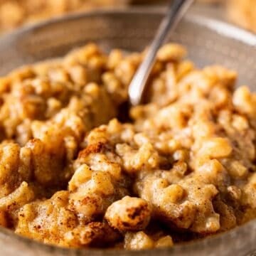 Pumpkin rice pudding in a glass bowl with a silver spoon and cinnamon topping.