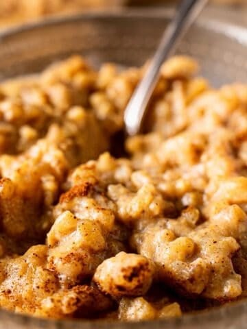 Pumpkin rice pudding in a glass bowl with a silver spoon and cinnamon topping.