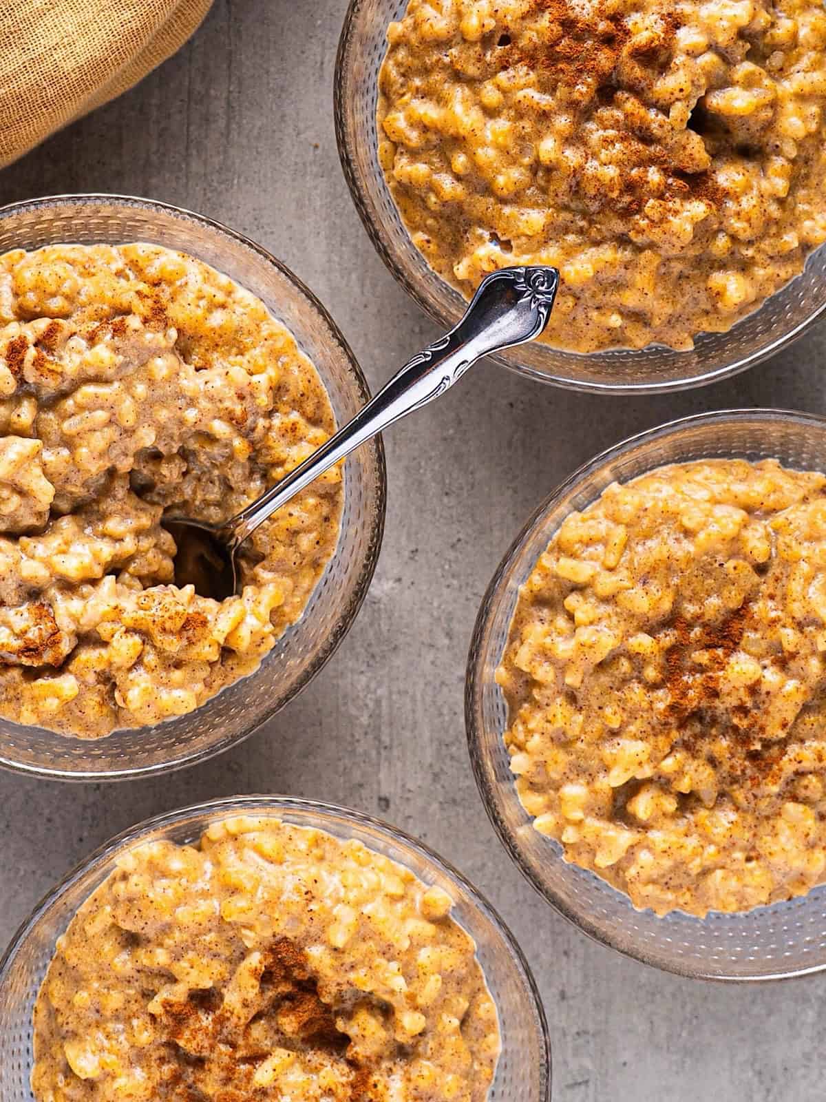 Four glass bowls of pumpkin rice pudding with a fall linen.