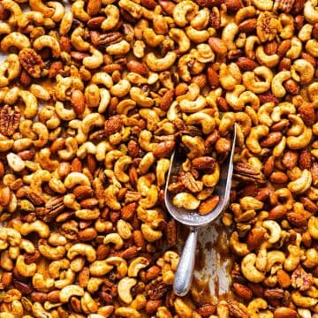 Sweet and spicy mixed nuts on sheet pan with parchment paper and a scooper.