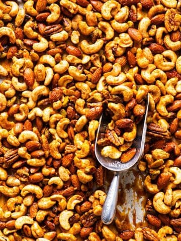 Sweet and spicy mixed nuts on sheet pan with parchment paper and a scooper.