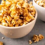 Two white bowls of caramel popcorn with spillover.