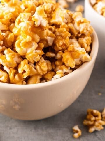 Two white bowls of caramel popcorn with spillover.