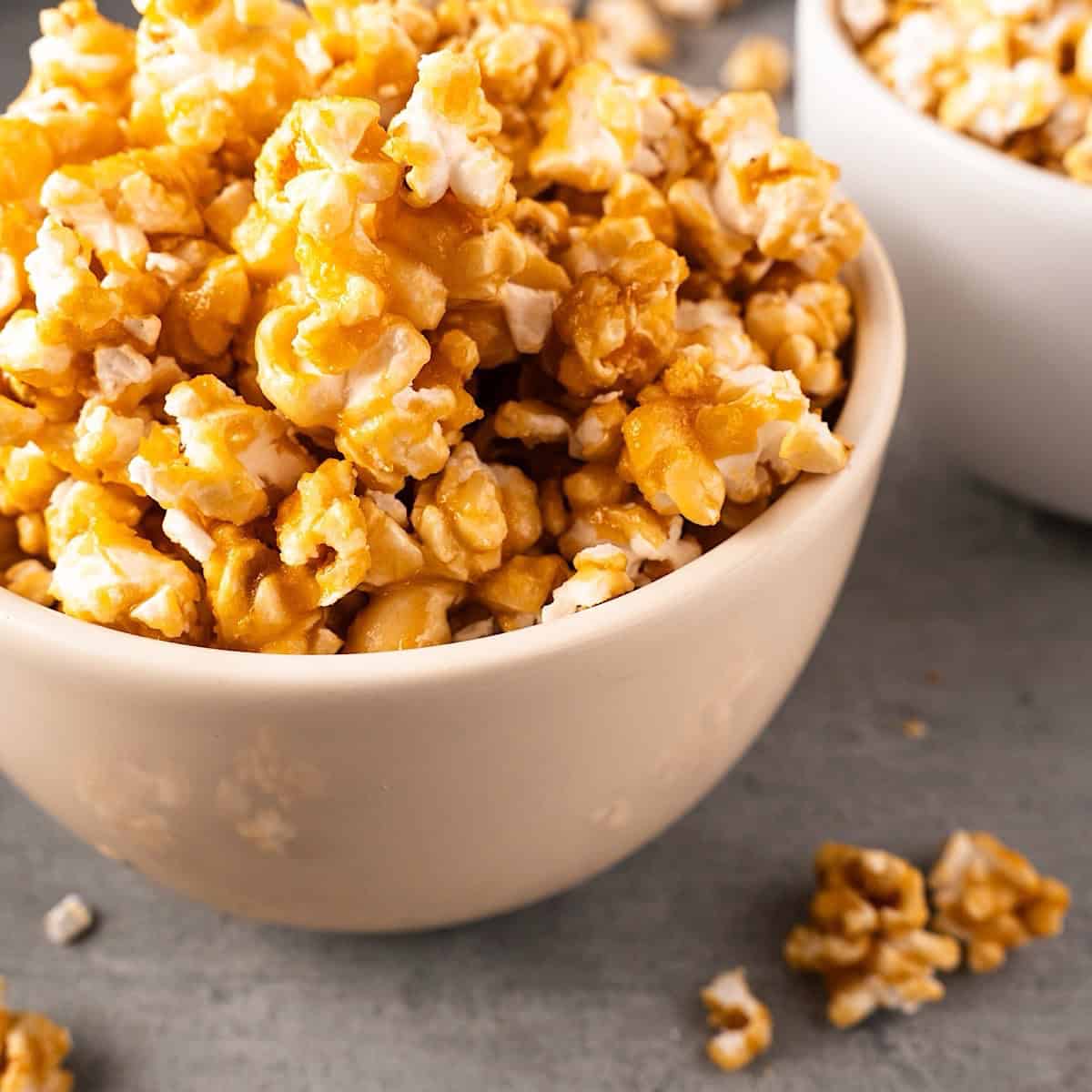 Two white bowls of caramel popcorn with spillover.