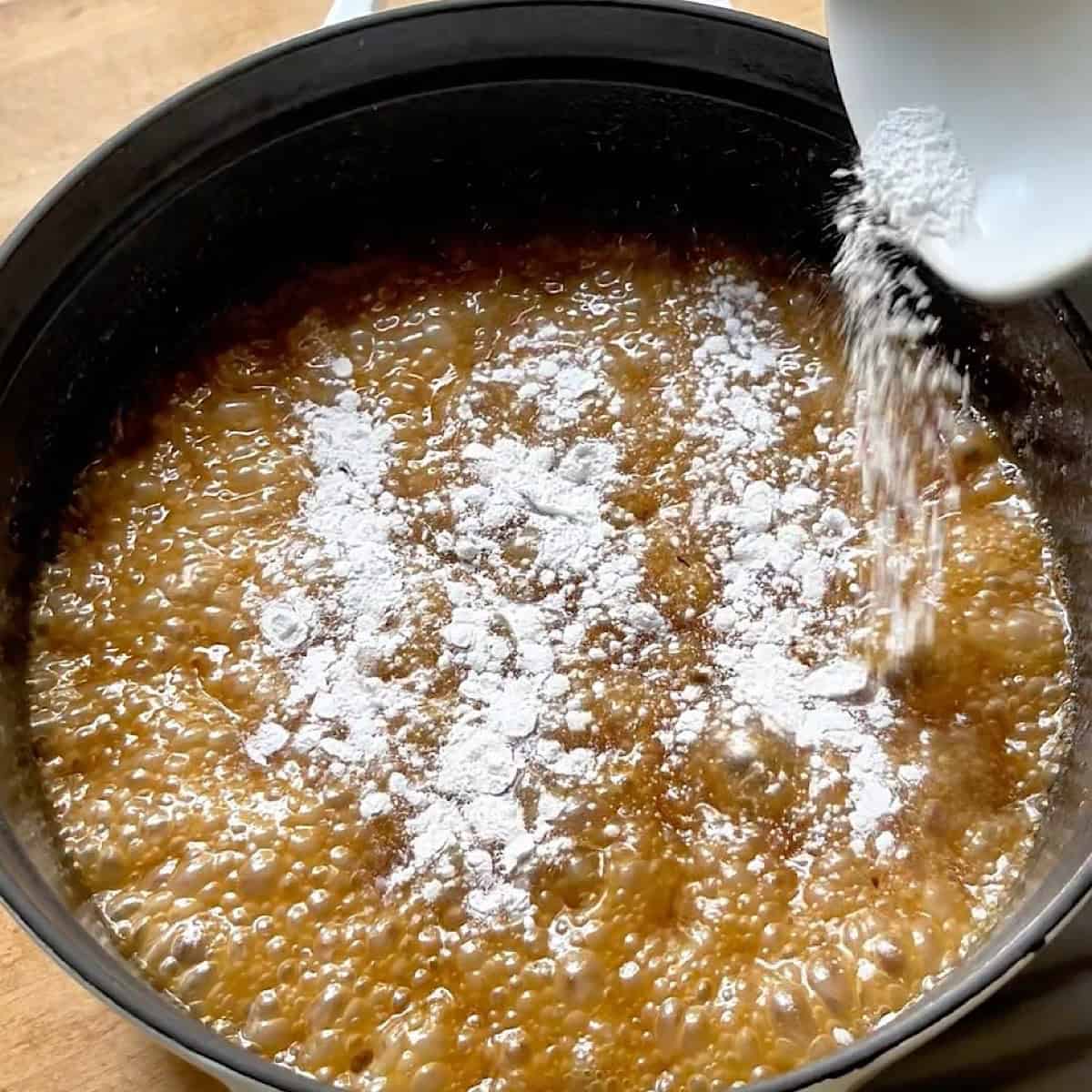 Adding baking soda to the boiling caramel in a pan.