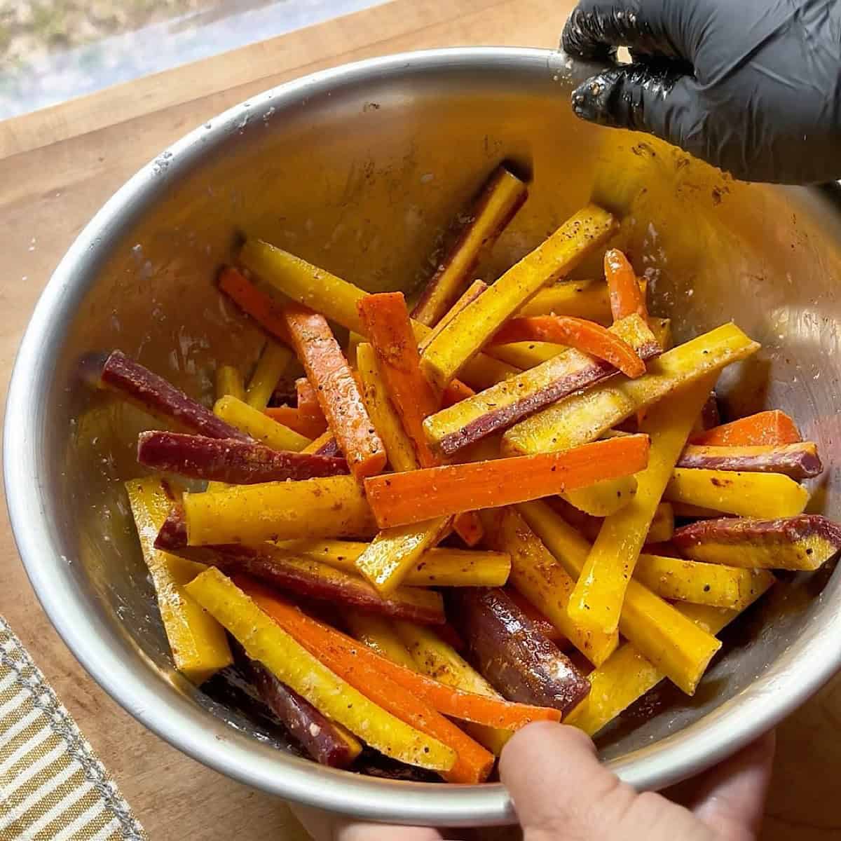 Seasoning and coating the rainbow carrots with spices and oil in a mixing bowl.