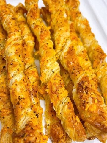 Cheese twists with puff pastry on a white serving platter.