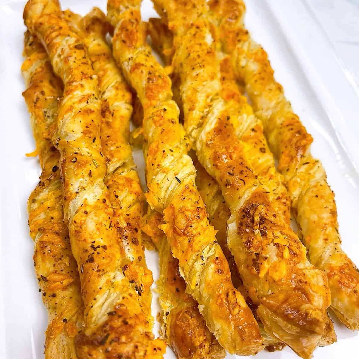 Cheese twists with puff pastry on a white serving platter.