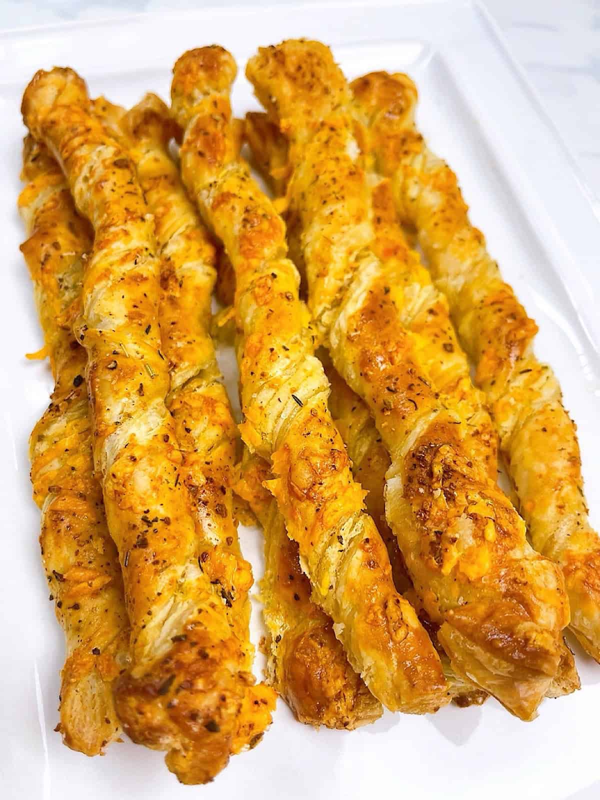 Cheese twists with puff pastry on a white serving platter.