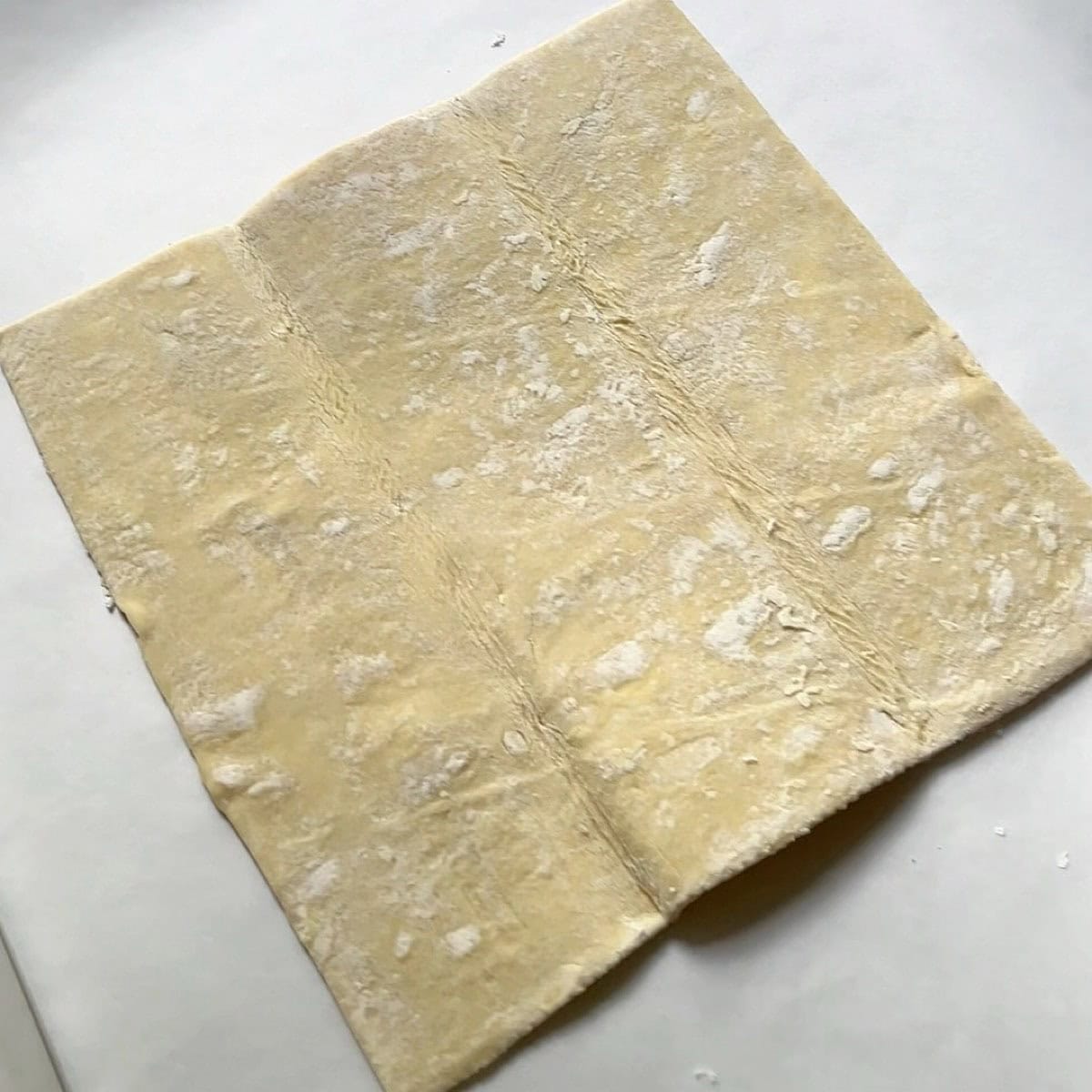 Puff pastry dough on parchment covered sheet pan unfolded.