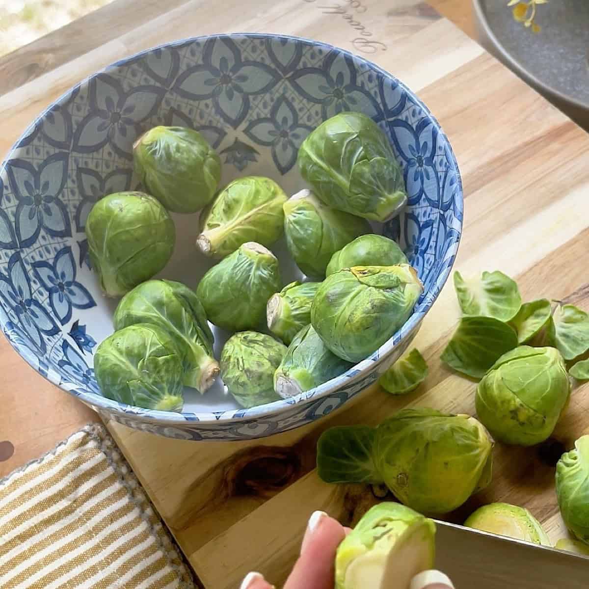 Trimmed brussels on a cutting board with a bowl.