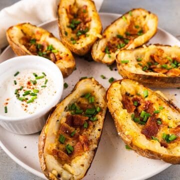 Crispy potato skins with cheese on a serving plate with garnish and sour cream.