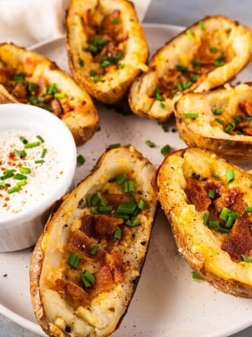 Crispy potato skins with cheese on a serving plate with garnish and sour cream.