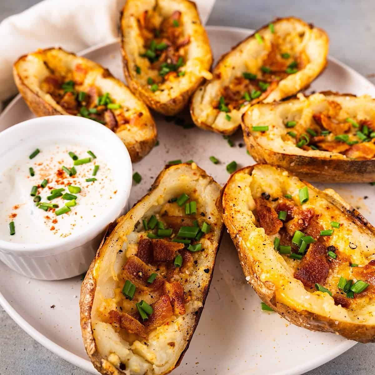 Crispy potato skins with cheese on a serving plate with garnish and sour cream.