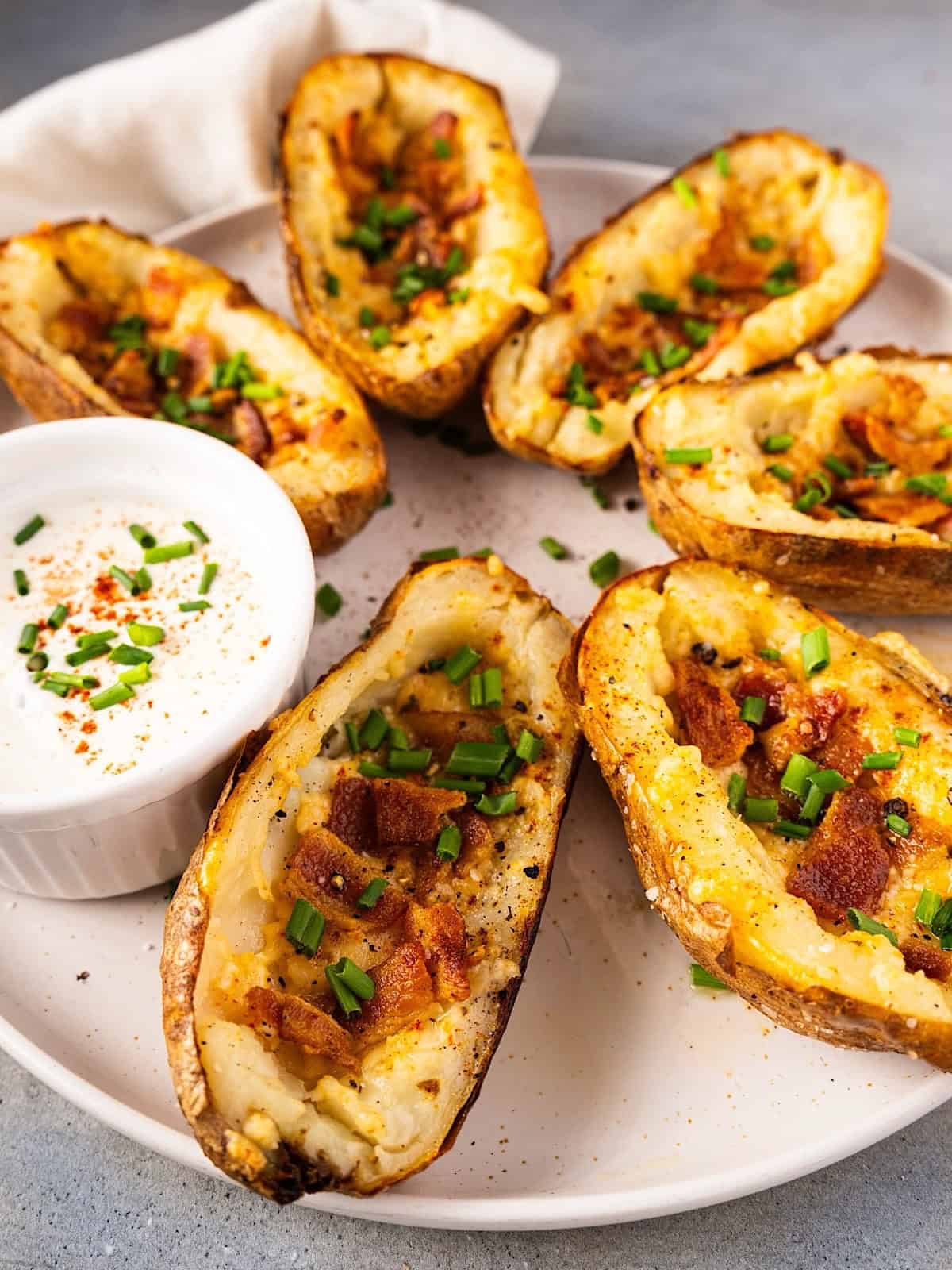 Crispy potato skins with cheese on a serving plate with garnish and sour cream.