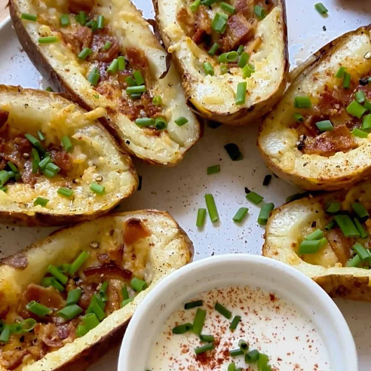 Crispy potato skins on a serving plate with sour cream, chives, and paprika.