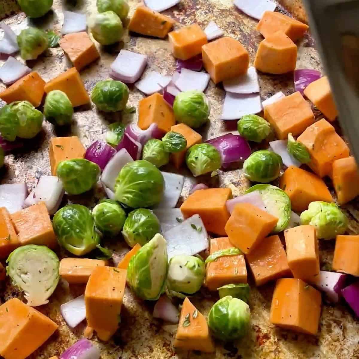 Prepared veggies tossed in oil and seasoning on a sheet pan.