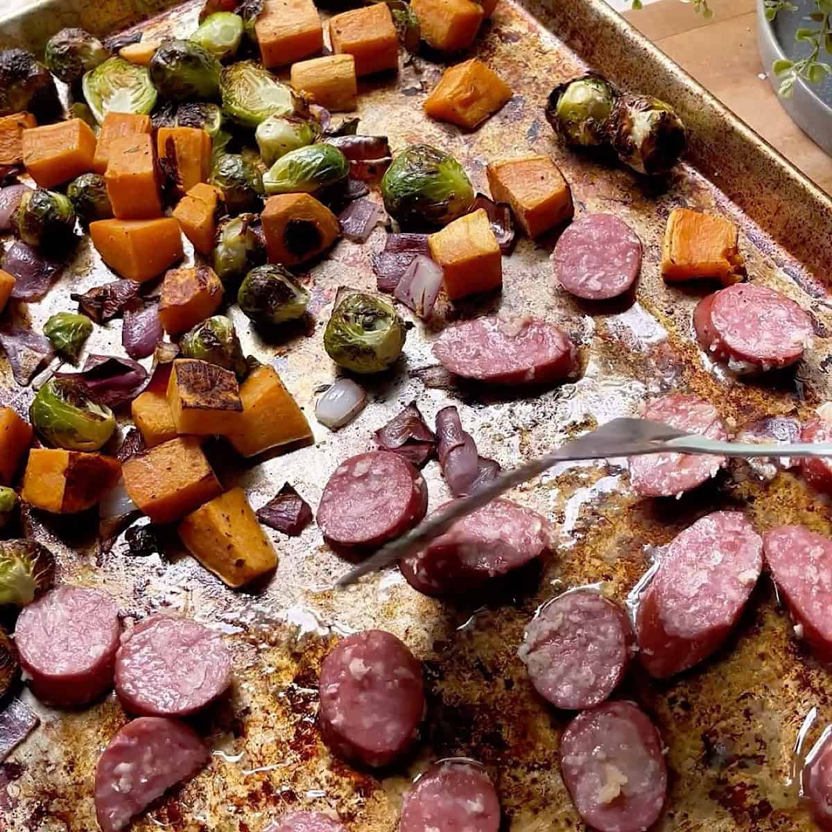 Sheet pan with vegetables on one side and sausage on the other.