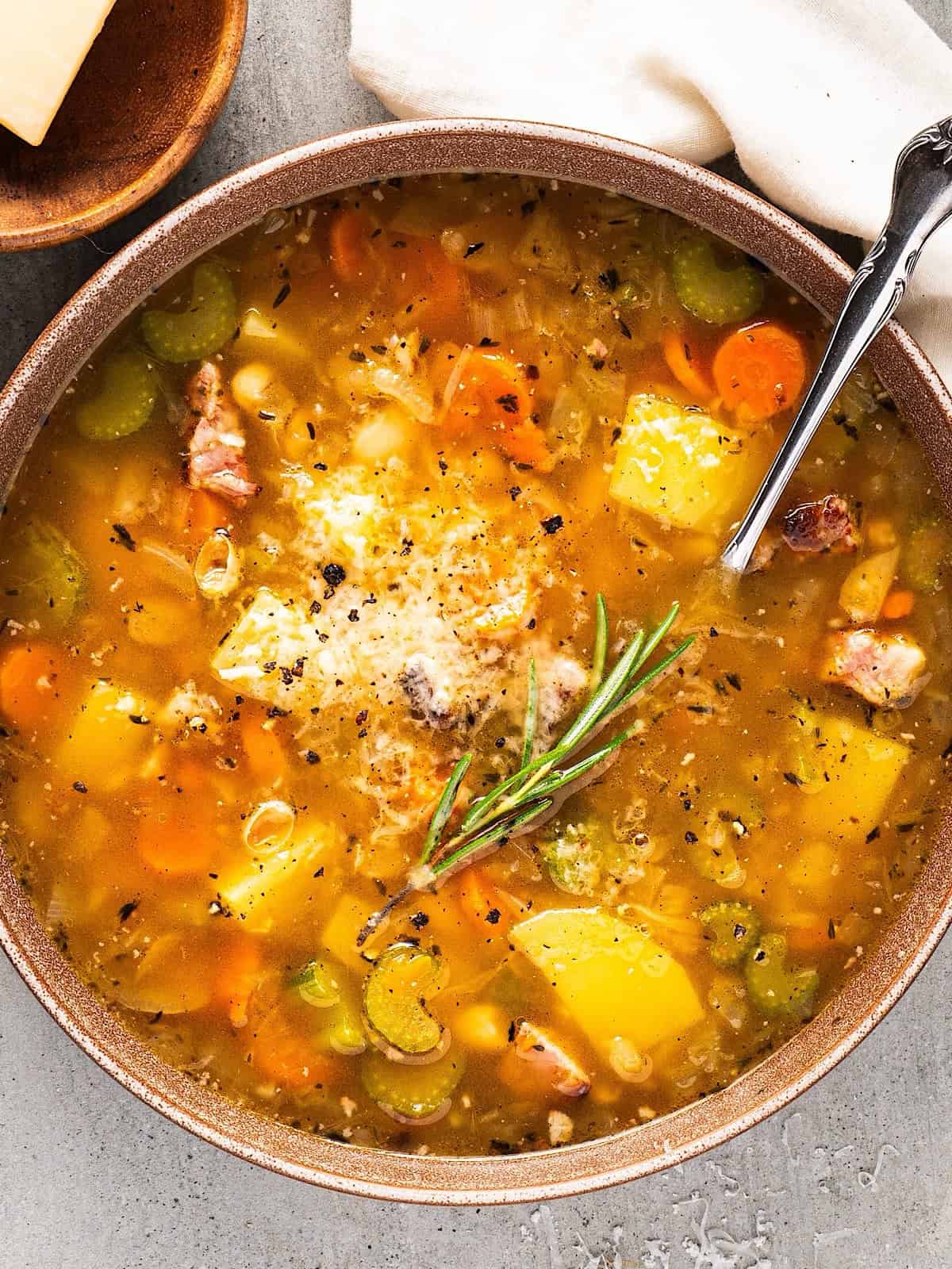 Italian white bean soup in a bowl with a spoon placed next to linen and parmesan rind.