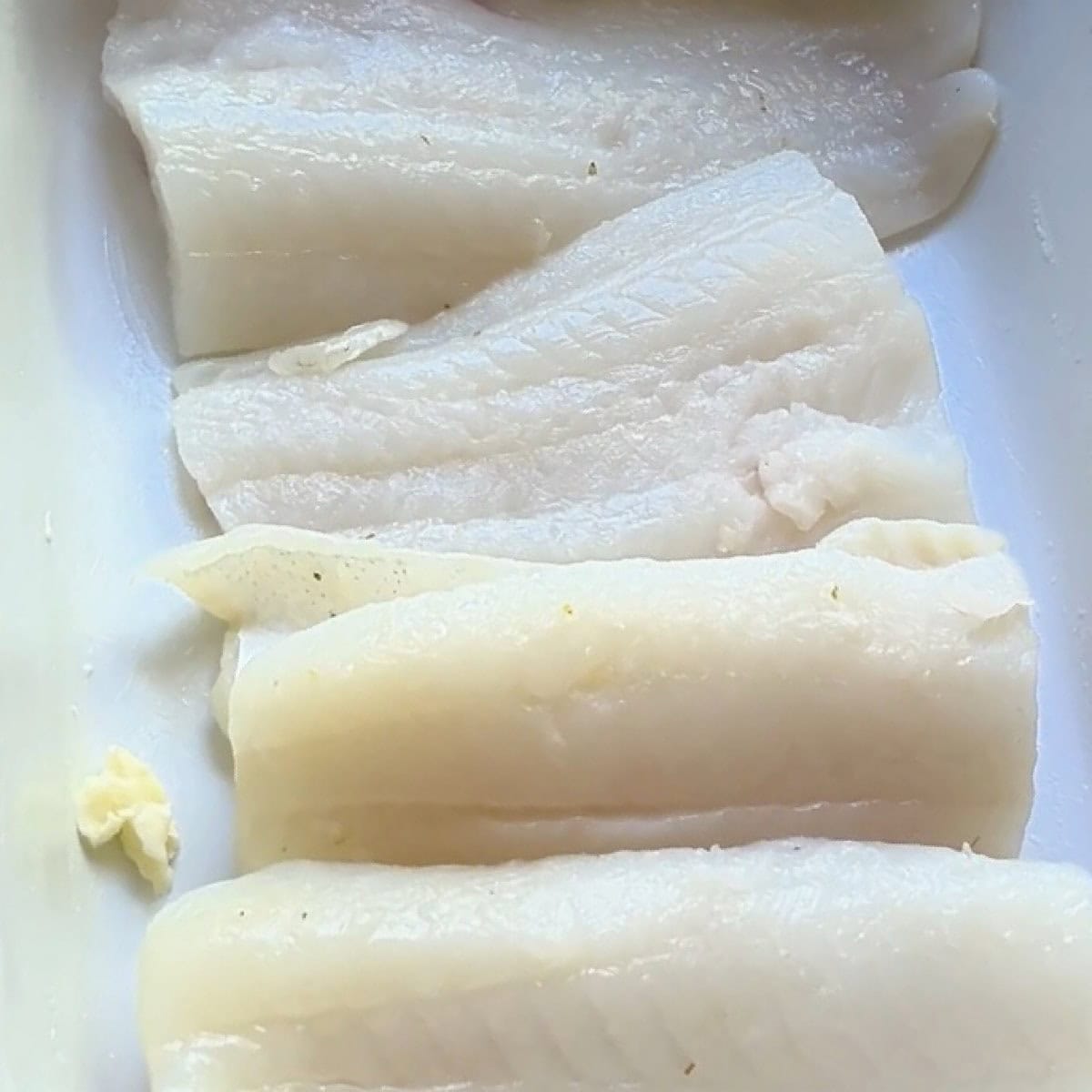 A buttered baking dish with four cod fillets.