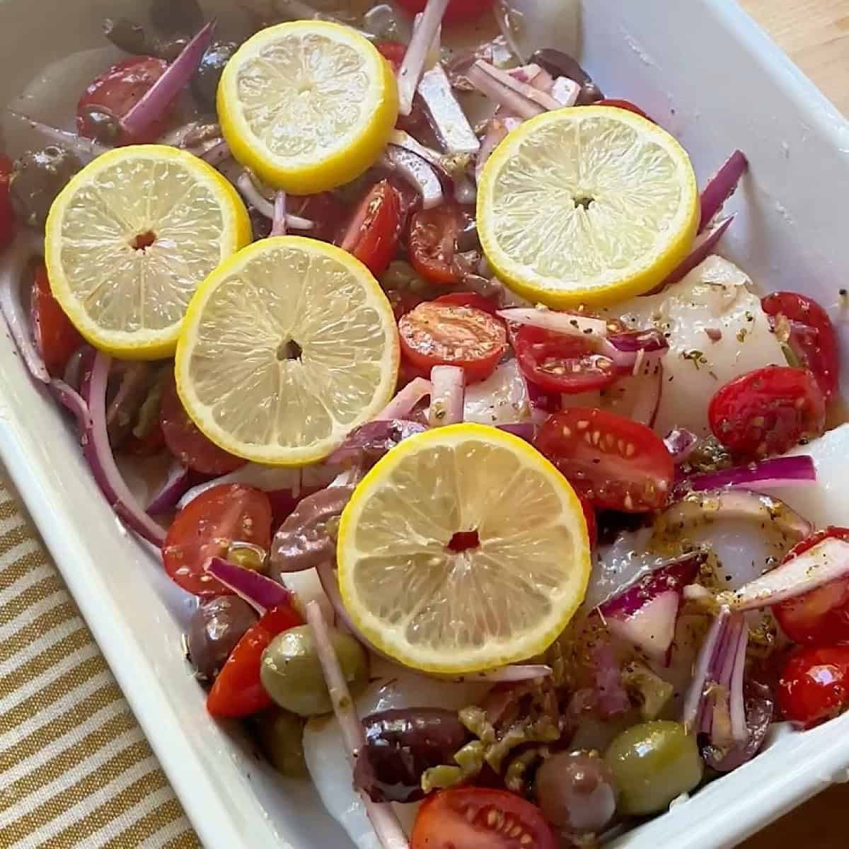 Mediterranean toppings and lemon slices on top of fish.
