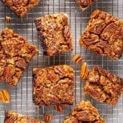 Clean cut pecan pie bars on wire rack with scattered pecan bits.