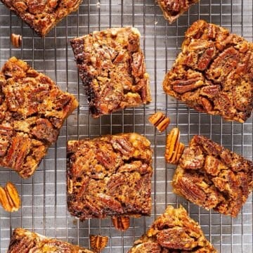 Clean cut pecan pie bars on wire rack with scattered pecan bits.
