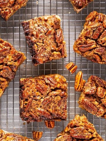 Clean cut pecan pie bars on wire rack with scattered pecan bits.