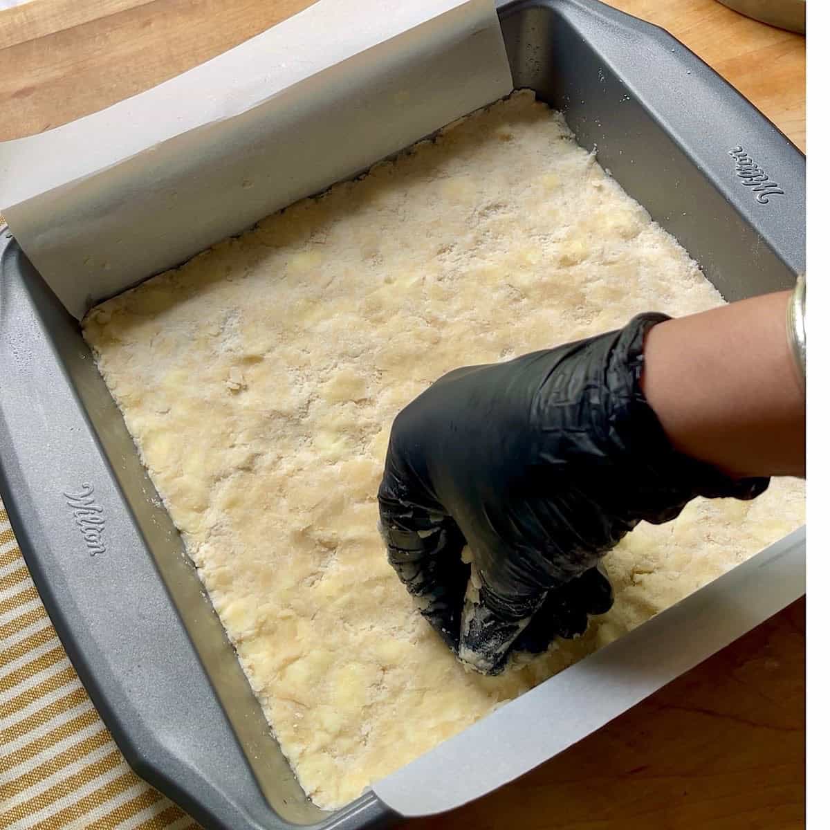 Pressing the shortbread crust into the parchment lined pan.