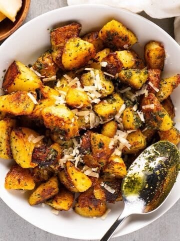 Pesto potatoes in a white bowl with a spoon, linen, and small bowl of parmesan.