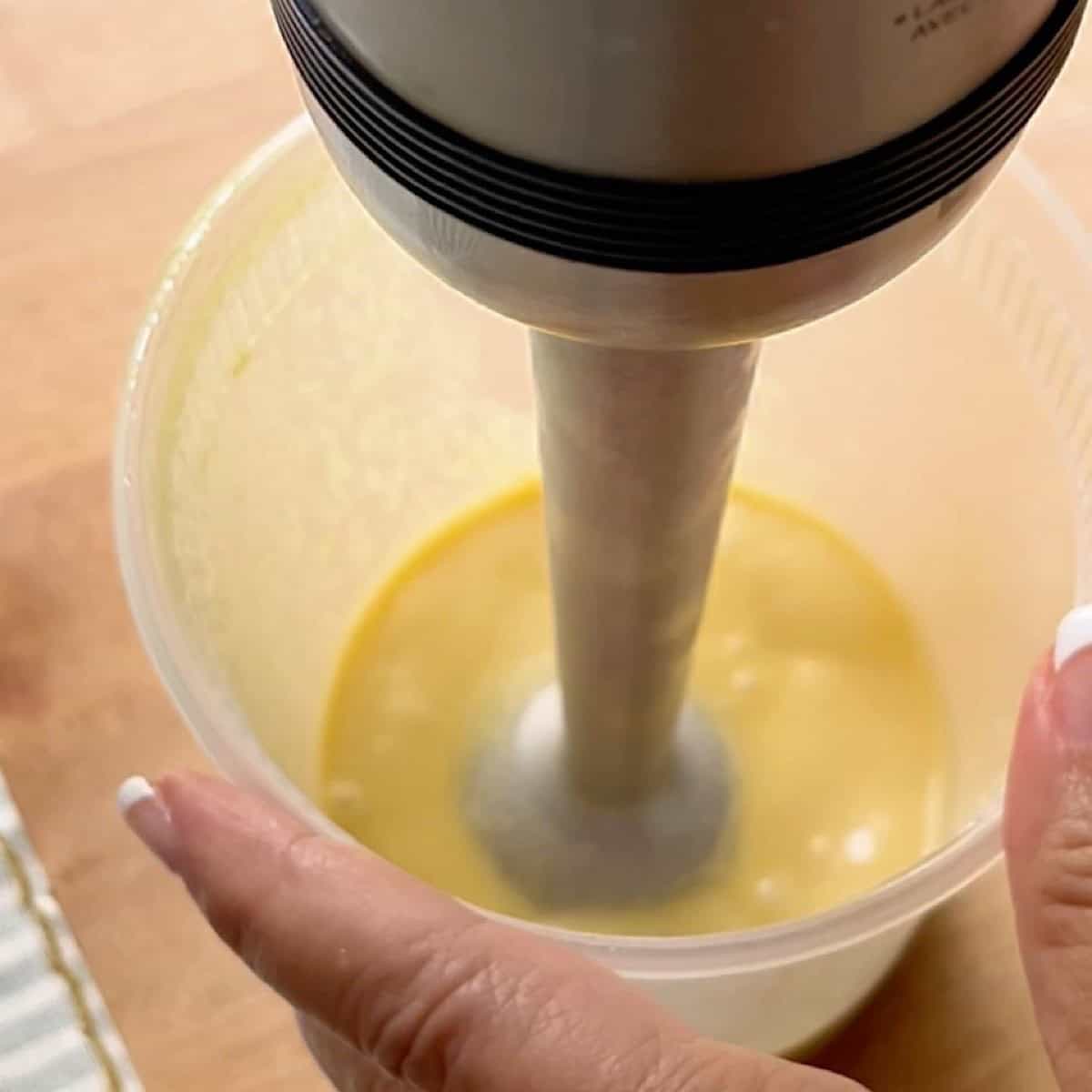 Caesar dressing being blended in a cup with an immersion blender.