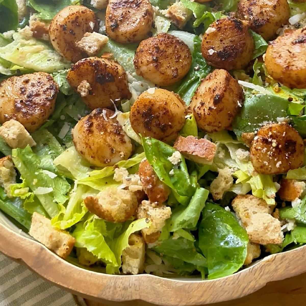 Scallop salad with seared blackened scallops on top in a serving bowl.