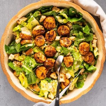 Tossed callop salad in a large salad bowl with salad tongs and linen on the side.