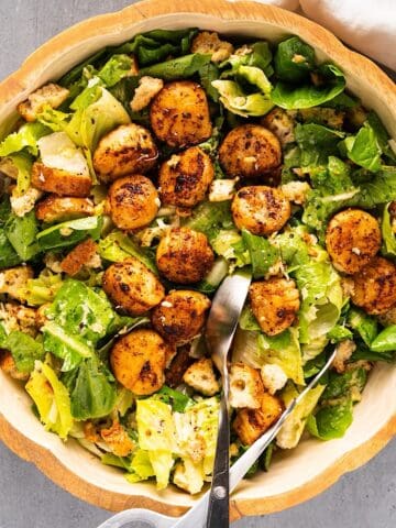 Tossed callop salad in a large salad bowl with salad tongs and linen on the side.