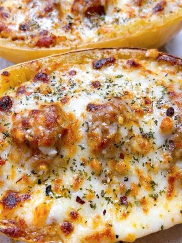 Two cheesy spaghetti squash halves loaded with marinara sauce and meatballs.