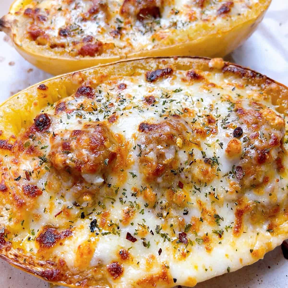 Two cheesy spaghetti squash halves loaded with marinara sauce and meatballs.