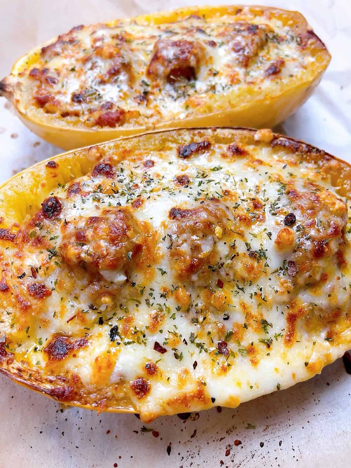Two cheesy spaghetti squash halves loaded with marinara sauce and meatballs.