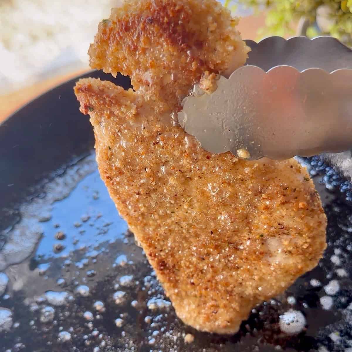 Searing the coated chicken in skillet to brown.