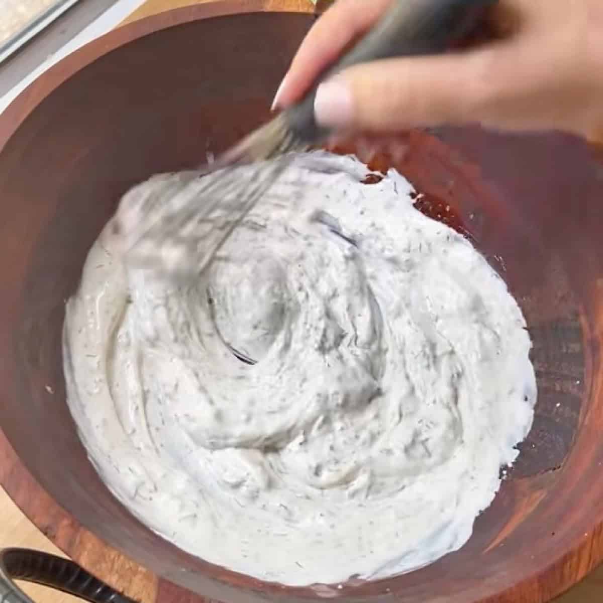 Whisking the Greek yogurt dressing in a salad bowl.