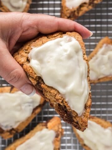 Holding a cinnamon roll scone with cream cheese glaze over a wire rack with remaining scones.