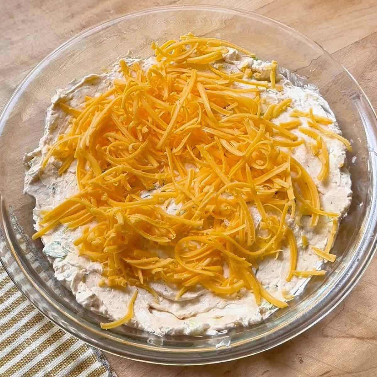 Layering cheese over the cream cheese base in a glass pie plate.